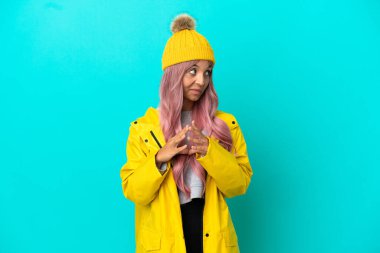 Pembe saçlı, yağmura dayanıklı bir ceket giyen genç bir kadın mavi arka planda bir şeyler planlıyor.