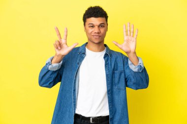 Sarı arka planda izole edilmiş genç Afrikalı Amerikalı sekiz parmaklı sayıyor.