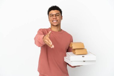 Beyaz arka planda izole edilmiş hamburger ve pizza tutan genç Afrikalı Amerikalı adam iyi bir anlaşma yaptığı için el sıkışıyor.
