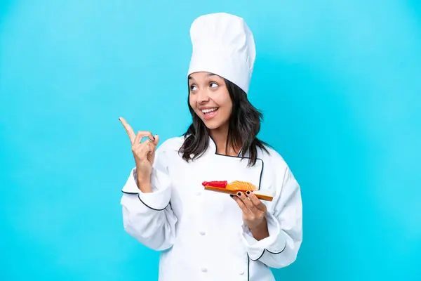 Young hispanic chef woman holding sashimi isolated on blue background intending to realizes the solution while lifting a finger up