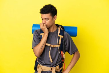 Sarı arka planda izole edilmiş büyük bir sırt çantası olan genç dağcı Afrikalı Amerikalı bir adam.