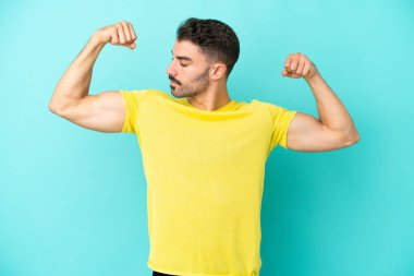 Mavi arka planda izole genç beyaz adam güçlü bir jest yapıyor.