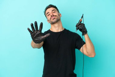 Genç dövme sanatçısı mavi arka planda izole edilmiş, parmaklarıyla beşi sayıyor.