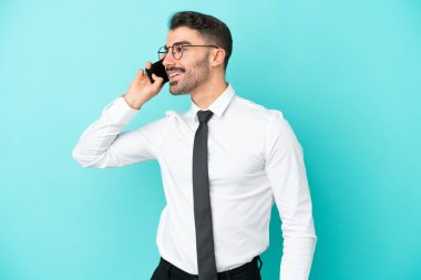 Kafkasyalı iş adamı mavi arka planda izole edilmiş cep telefonuyla sohbet ediyor.