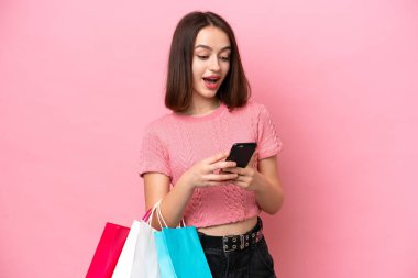 Genç Ukraynalı bir kadın pembe arka planda izole edilmiş. Elinde alışveriş çantaları var ve bir arkadaşına cep telefonuyla mesaj yazıyor.