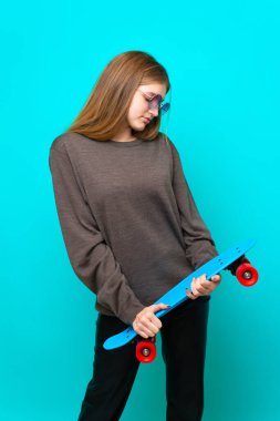 Genç kaykaycı kız mavi arka planda izole edilmiş.