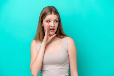 Teenager Russian girl isolated on blue background whispering something with surprise gesture while looking to the side