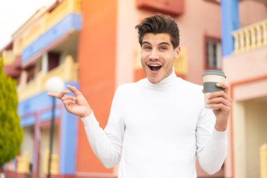 Kafkasyalı genç bir adam açık havada kahve tutuyor. Şaşırmış ve parmağıyla işaret ediyor.