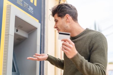 Açık havada ATM kullanan genç beyaz bir adam.
