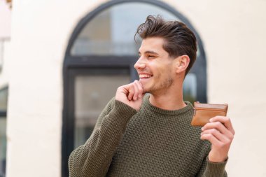 Kafkasyalı genç bir adam dışarıda bir cüzdan tutuyor bir fikir üretiyor ve bakıyor.