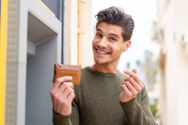 Açık havada ATM kullanan genç beyaz bir adam.