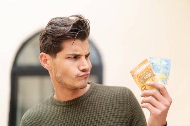 Kafkasyalı genç adam üzgün bir ifadeyle dışarıda çok para alıyor.