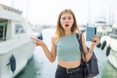 Açık havada elinde pasaportu olan genç sarışın kadın şaşırmış ve işaret ediyor.