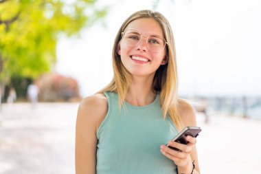 Açık havada cep telefonu kullanan genç sarışın kadın.
