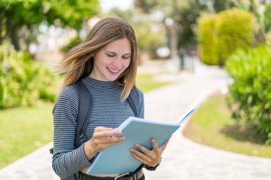 Açık havada elinde bir defter tutan sarışın genç bir kadın.