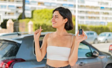 Dışarıda arabanın anahtarlarını tutan genç ve güzel Bulgar kadın, çözümün farkına varmak için parmağını kaldırıyor.