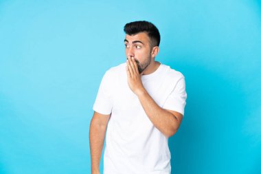 Kafkasyalı bir adam mavi arka planda, yan tarafa bakarken sürpriz hareketlerle bir şeyler fısıldıyor.