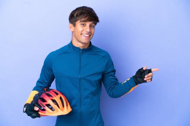 Mor arka planda izole edilmiş genç bir beyaz adam, parmağını yana doğru gösteriyor.