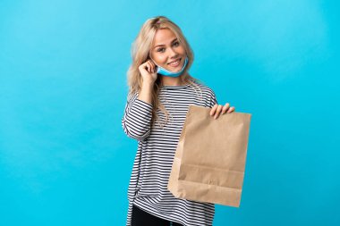 Young Russian woman holding a grocery shopping bag isolated on blue background laughing
