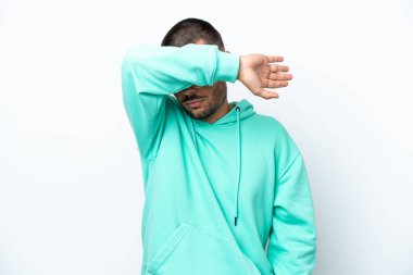 Beyaz arka planda izole edilmiş beyaz tenli genç adam gözlerini elleriyle kapatıyor.