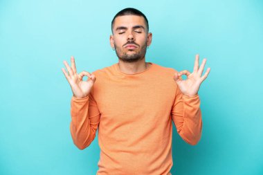 Zen pozisyonunda mavi arka planda izole edilmiş genç beyaz bir adam.