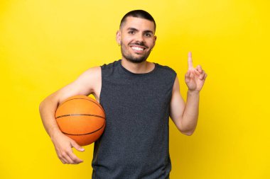 Young caucasian basketball player man isolated on yellow background pointing up a great idea