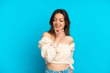 Mavi arka planda soyutlanmış genç beyaz kadın yana bakıyor ve gülümsüyor.