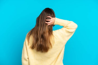 Kafkasyalı genç bir kadın mavi arka planda izole edilmiş ve düşünüyor.