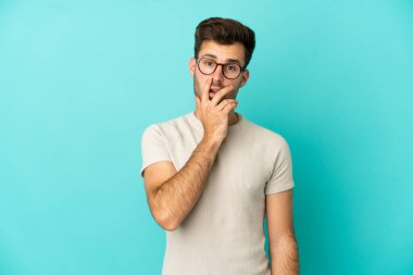 Mavi arka planda izole edilmiş beyaz, yakışıklı genç adam sağa bakarken şaşırmış ve şok olmuştu.