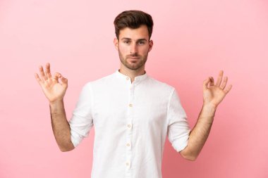 Zen pozisyonunda pembe arka planda izole edilmiş beyaz yakışıklı bir adam.