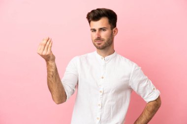 Pembe arka planda izole edilmiş beyaz, yakışıklı genç bir adam İtalyan jesti yapıyor.