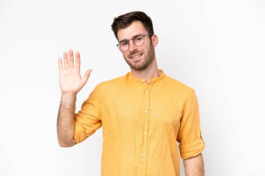 Beyaz arka planda izole edilmiş genç beyaz bir adam mutlu bir ifadeyle selamlıyor.