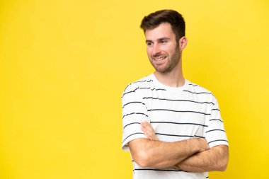 Sarı arka planda izole edilmiş, kolları çapraz ve mutlu genç beyaz bir adam.