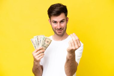 Kafkasyalı genç adam çok para alıyor. Sarı arka planda izole edilmiş. Para hareketi yapıyor.