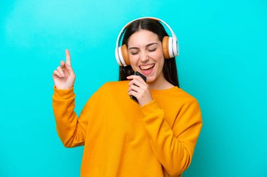 Mavi arka planda izole edilmiş genç bir kız cep telefonuyla müzik dinliyor ve şarkı söylüyor.