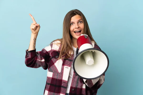Young Slovak woman isolated on blue background shouting through a megaphone and pointing side