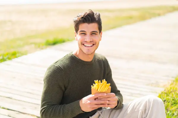 Joven Hombre Caucásico Sosteniendo Patatas Fritas Aire Libre Sonriendo Mucho —  Fotos de Stock