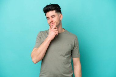 Kafkasyalı genç adam mavi arka planda izole edilmiş, yana bakıyor ve gülümsüyor.