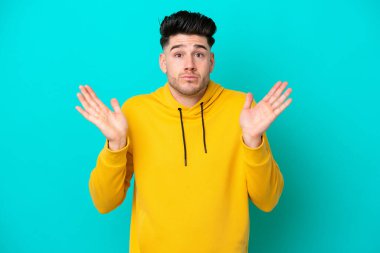 Mavi arka planda izole edilmiş genç beyaz adam şüpheli hareketler yapıyor.