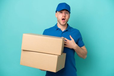 Teslimat yapan beyaz adam mavi arka planda izole edildi. Şaşırdı ve şaşırdı.