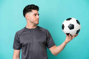 Yakışıklı genç futbolcu mavi arka planda izole edilmiş.