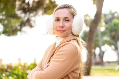 Sarışın genç bir kadın açık havada kolları bağlı ve ileriye bakıyor.