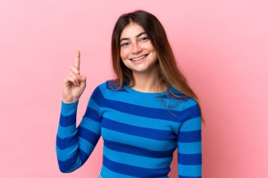 Pembe arka planda izole edilmiş genç beyaz kadın en iyinin işareti olarak parmağını kaldırıyor.