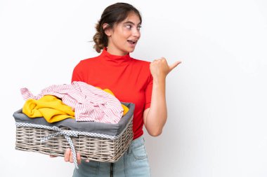 Beyaz arka planda izole edilmiş çamaşır sepeti tutan beyaz bir kadın bir ürünü sunmak için kenarı işaret ediyor.