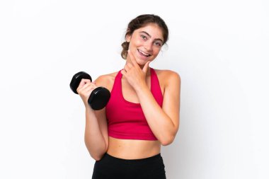 Beyaz arka planda halter kaldıran genç beyaz kadın mutlu ve gülümsüyor.