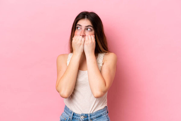 Young caucasian woman isolated on pink background nervous and scared putting hands to mouth