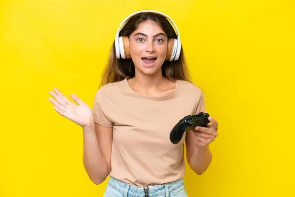 stock image Young caucasian woman playing with a video game controller isolated on yellow background with shocked facial expression