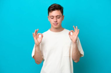 Genç ve yakışıklı Brezilyalı bir adam Zen pozunda mavi arka planda izole edilmiş.