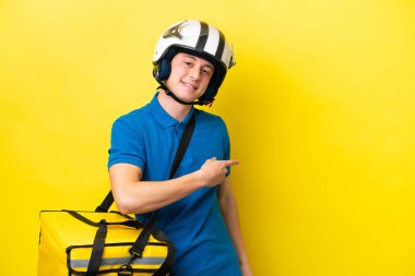 Sırt çantalı genç Brezilyalı adam sarı arka planda izole edilmiş, parmağıyla kenarı işaret ediyor.