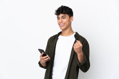 Genç adam izole edilmiş beyaz arka planda ve telefon zafer pozisyonunda.